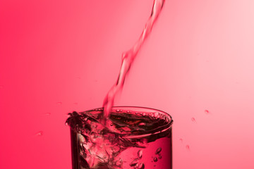 Chorro de agua entrando en un vaso lleno de agua produciendo un chapoteo y burbujas, cayendo gotas...