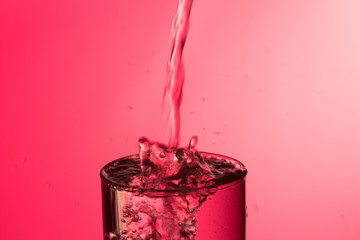 Chorro de agua entrando en un vaso lleno de agua produciendo un chapoteo y burbujas, cayendo gotas de agua fuera