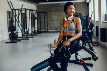 Beautiful black girl in the gym. A woman in a gray top. Lady with a headphones
