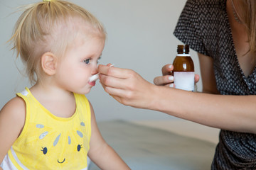 Mother giving daughter medicine on a spoon. Flu, fever or coughing symptoms. Mother giving a spoon...