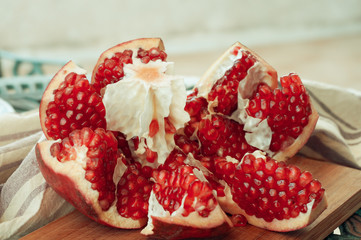 Cut red juicy pomegranate on wooden board linen towel on background