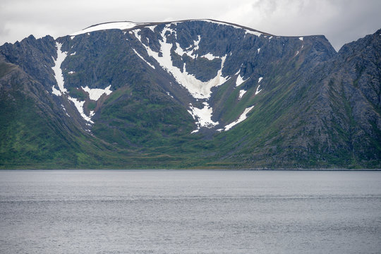 summer snow on steep slopes near fjord waters on Soroya island, Norway