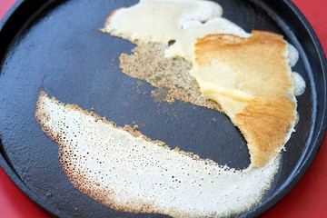 Pancake stuck to a pan for baking pancakes. A thin pancake stuck to the pan. The first pancake is lumpy.