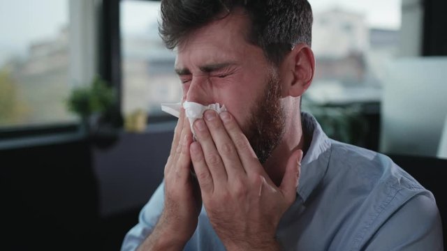 Sick office manager suffering bad allergic feeling sneezing using paper tissues trying to work. Overworked employee portrait.
