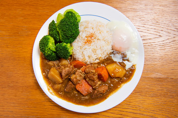 Pork Curry Rice on wooden background ( Onsen tamago, Potato, enoki mushroom, onion, broccoli, Japanese style,)