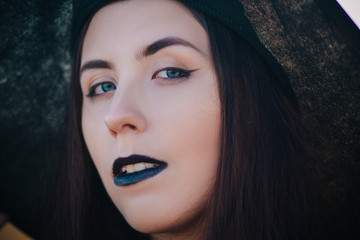 Portrait young, beautiful girl with pale skin and black lips in the form of a witch for Halloween. A model with clean skin.