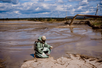 A scientist takes a sample of water after the release of chemical waste. A man in a respirator and...