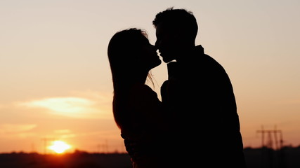 Silhouette of first tenderly kissing of adorable young couple in the field at sunset