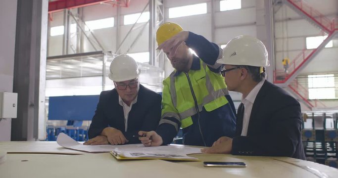 Two engineers in formal suits and workman in uniform on meeting. Technician in helmet explain gesturing the process and data