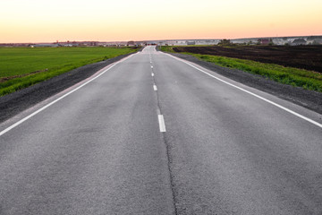 the asphalt road stretching away into the distance on the horizon shows the sunset sky and fog