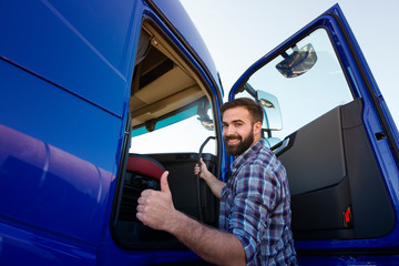 Professional truck driver entering his truck long vehicle and holding thumbs up. Loving his job....