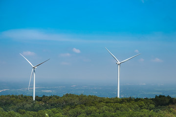 The big white wind turbine for spinning electricity sees large mountains far away, with clouds and blue skies above the mountains.
