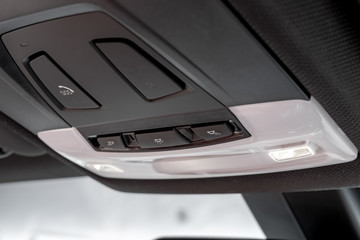 Close-up, isolated view of an emergency SOS call button together with lighting buttons seen in the roofline of a luxury, german-made sports car at a showroom.