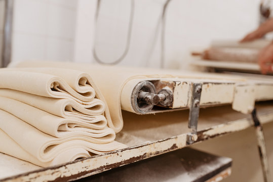 Shabby machine rolling fresh soft dough for pastry preparation in kitchen of professional bakery