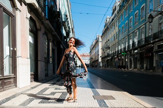 Playful woman in long dress turning around while walking along city summer street
