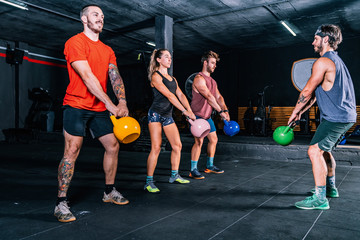 Muscular fellows with coach lifting up kettle bells while functional training in contemporary health club