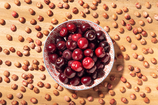 Top view of fresh sweet cherries in bowl with cherry seeds around on wooden table
