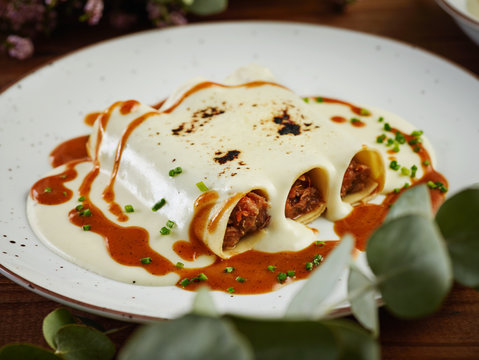 Closeup hake and txangurro cannelloni with oxtail served with bechamel sauce on ceramic plate