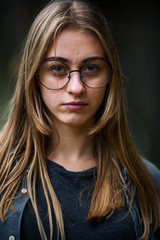 Teenager. Young beautiful white caucasian teenage girl in casual clothes and glasses on the street in the dark forest in the autumn evening. Close up.