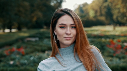 Portrait of cheerful beautiful calm woman with red hair looking at camera at sunny park
