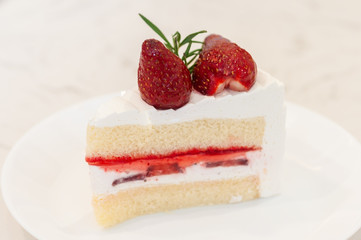 A piece of strawberry cake with cream and strawberry jam layers and topping with two fresh strawberry.