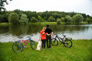Влюбленная пара с собакой в парке у пруда после велопрогулки