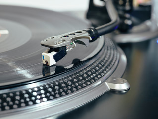 Closeup of top of old black turntable with tonearm maintaining position of cartridge tracing groove and playing LP record