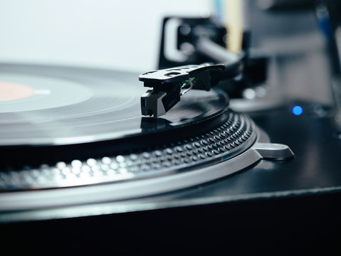Closeup of top of old black turntable with tonearm maintaining position of cartridge tracing groove and playing LP record