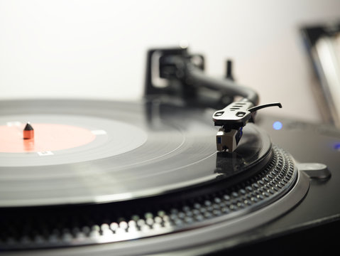Closeup of top of old black turntable with tonearm maintaining position of cartridge tracing groove and playing LP record