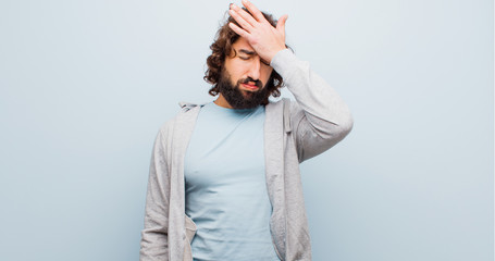 young bearded crazy man looking stressed, tired and frustrated, drying sweat off forehead, feeling hopeless and exhausted against flat color wall