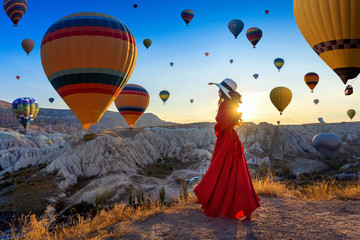 Beautiful girl standing and looking to hot air balloons in Cappadocia, Turkey. - obrazy, fototapety, plakaty