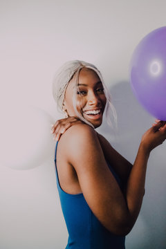 Joyful Black adult female with colorful balloons looking at camera while standing on white background