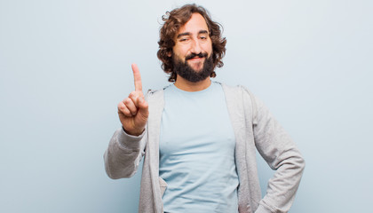 young bearded crazy man smiling and looking friendly, showing number one or first with hand...