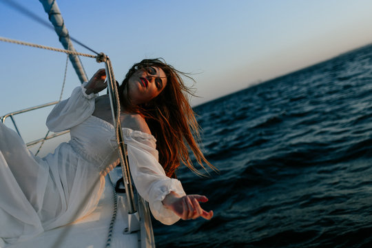 Tranquil woman in luxury white dress resting while lying on yacht during cruise with closed eyes