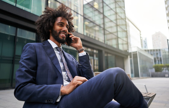 Joyful Ethnic Man In Suit Sitting Outside And Talking Phone