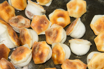 Dumplings fried in a black pan in vegetable oil