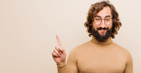 young bearded crazy man smiling cheerfully and happily, pointing upwards with one hand to copy space against flat color wall - obrazy, fototapety, plakaty