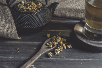 From above of dried daisy in spoon on dark wooden table near cup with herbal tea