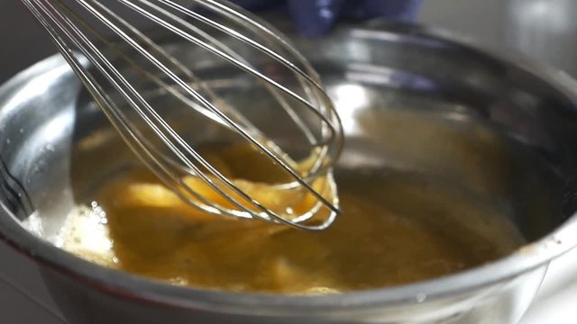 Girl whips the raw eggs with sugar in a glass bowl. Whisking the eggs