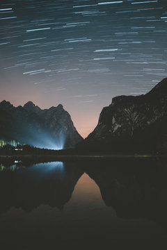 Blue rays of light shining at beautiful tranquil night with clear starry sky on lake in Dolomites mountains during fair weather