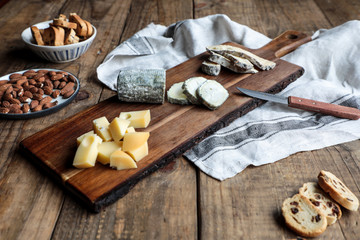 Sweet croutons with raisins and plate with almonds placed on wooden table near board with various cut cheese