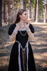 Portrait of a young, beautiful girl in a black medieval dress standing in a pine forest.