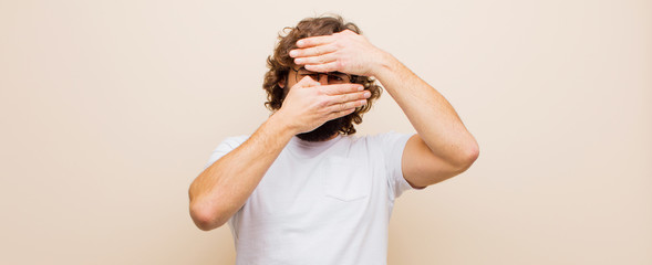 young bearded crazy man covering face with both hands saying no to the camera! refusing pictures or...