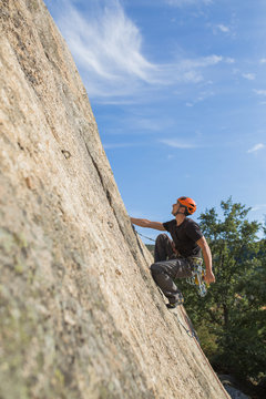 From below man climbing a rock in nature with climbing equipment