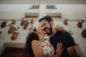 Low angle of loving casual couple having fun and cuddling while standing next to picturesque white building in summer town