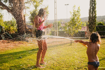 Excited teen girl laughing and playing with jet of clean water while having fun in garden on sunny day