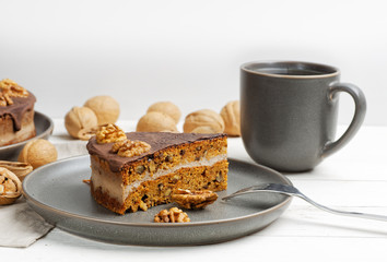 Piece of homemade walnut cake with chocolate icing and mug of tea on white wooden table. Shallow focus.