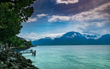 View of coastal stones, lake, mountain range and blue sky with clouds.Lake Geneva,mountain Alps in Montreux,canton Vaud Switzerland.