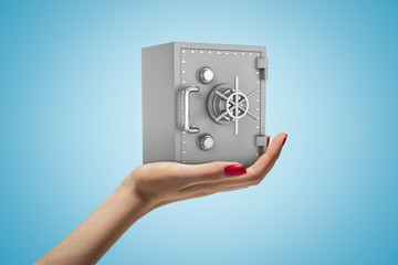 Close-up of woman's hand facing up and holding small grey money safe on light-blue background.
