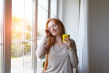 beautiful sleepy smiling young red haired girl with cup of her fresh morning coffee